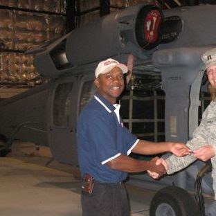 Two men shake hands in front of a helicopter inside a hangar.