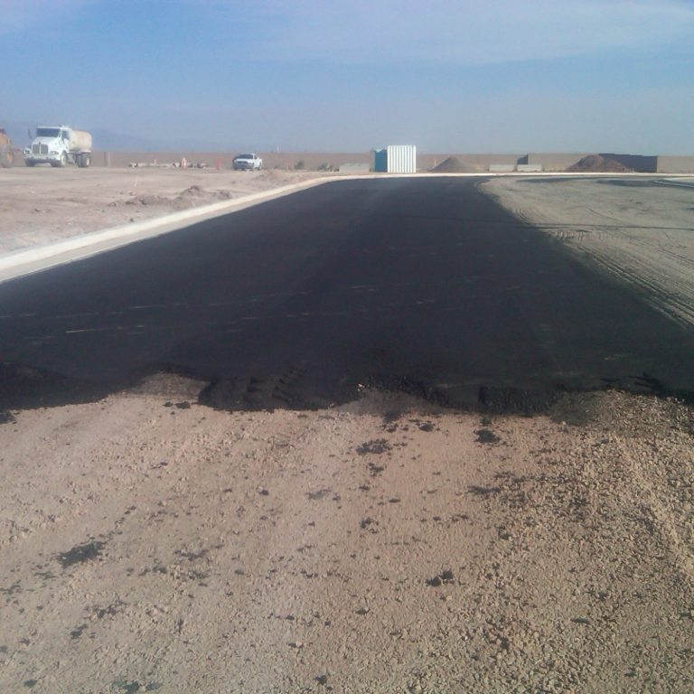 Recently paved black asphalt road in a barren landscape under a clear sky.